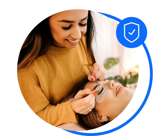 Female lash technician in a yellow jumper performing a lash treatment on a client.